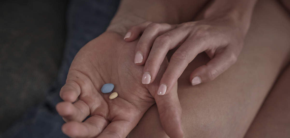 A man is holding ED pills in his hand, while his partner touches his hand